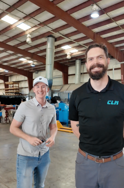 Two men smiling inside the CLN warehouse, one in a light shirt and cap and one in a CLN polo shirt