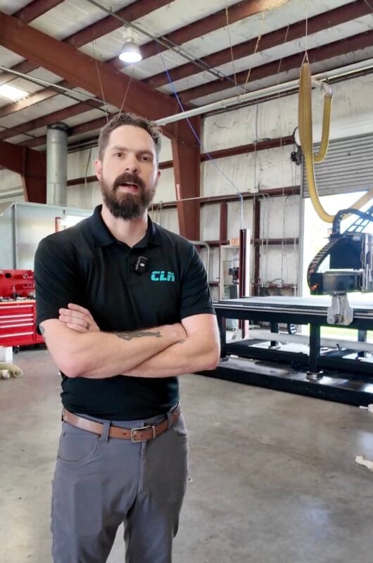 Man in a CLN polo shirt standing with arms crossed in front of a CNC machine inside the CLN of South Florida manufacturing facility