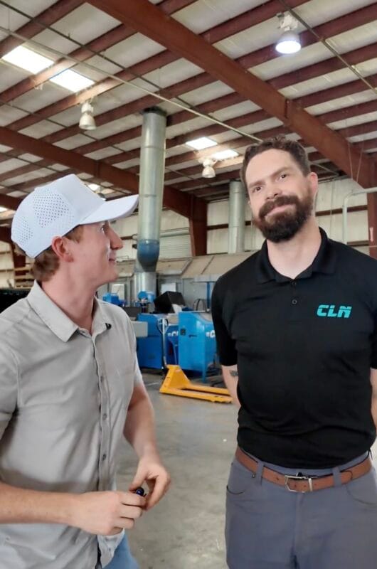 Rand Larsen in a CLN polo shirt talking with a visitor in a white cap on the CLN of South Florida factory floor