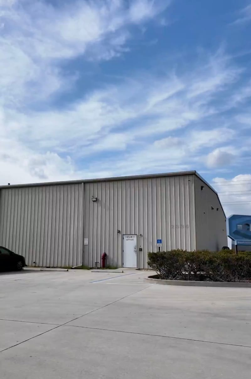 Exterior of the CLN office, a metal-sided warehouse building with a white entry door and CLN Office sign, parking lot in the foreground